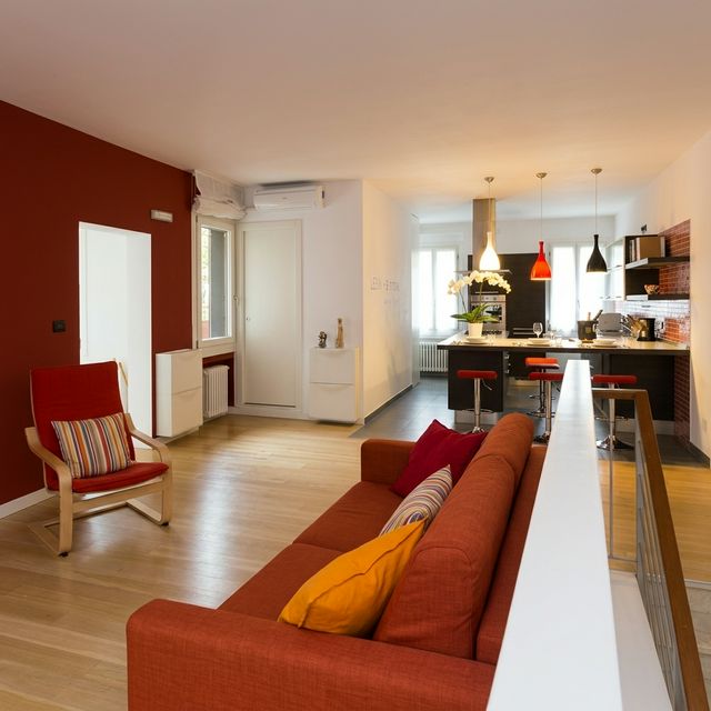 BRW House living room — panoramic open plan with sofa, red wall, black kitchen in the background